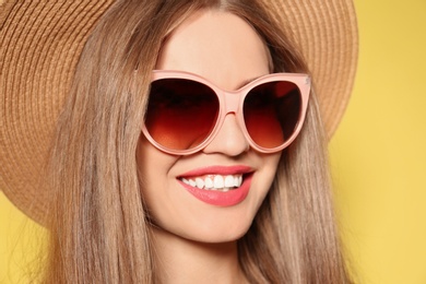 Photo of Young woman wearing stylish sunglasses and hat on yellow background