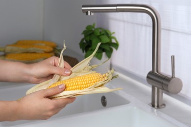 Woman husking corn cob in kitchen, closeup