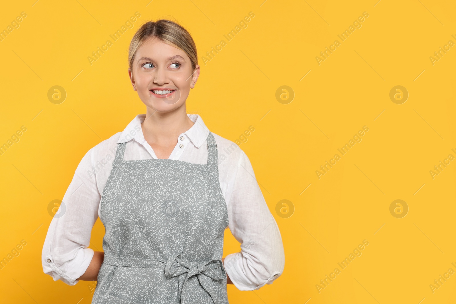 Photo of Beautiful young woman in clean apron with pattern on orange background. Space for text