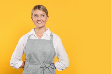 Beautiful young woman in clean apron with pattern on orange background. Space for text