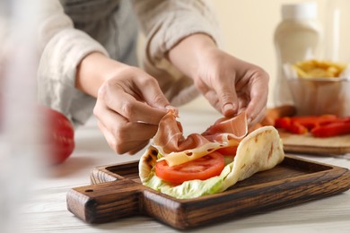 Photo of Woman cooking delicious pita wrap with jamon, cheese and vegetables at wooden table, closeup