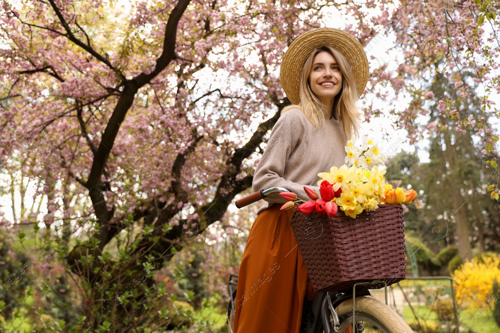 Photo of Beautiful young woman with bicycle and flowers in park on pleasant spring day. Space for text