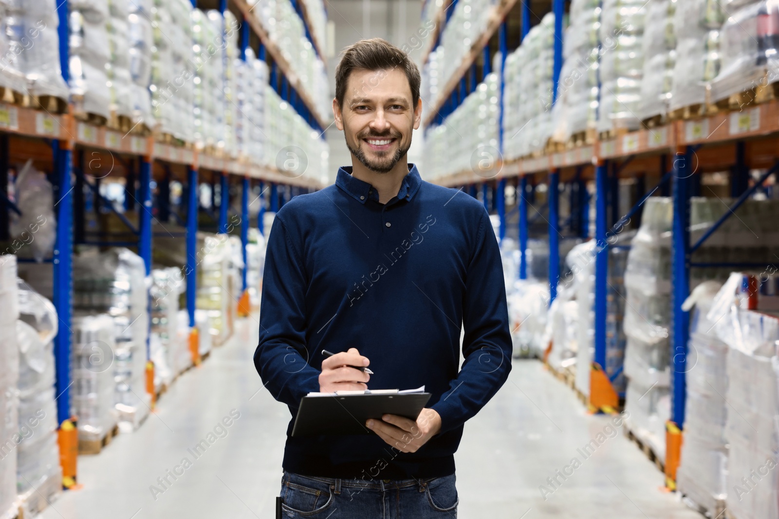 Photo of Happy manager holding clipboard in warehouse with lots of products