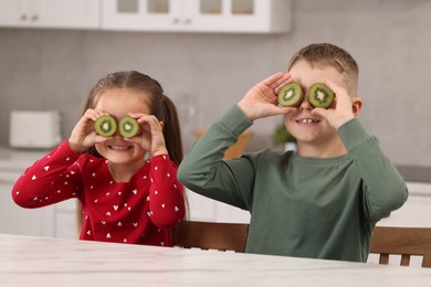 Photo of Happy children with fresh kiwis at table in kitchen