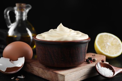 Photo of Fresh mayonnaise sauce in bowl and ingredients on black table, closeup