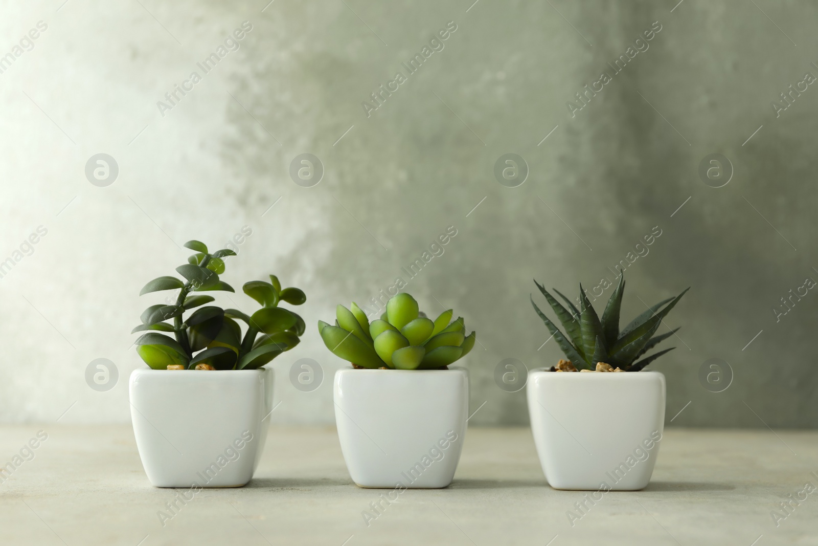 Photo of Artificial plants in white flower pots on light stone table