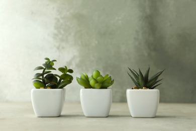 Artificial plants in white flower pots on light stone table