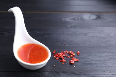 Photo of Chili sauce in spoon on black wooden table, closeup. Space for text