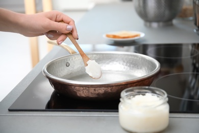 Photo of Woman putting coconut oil on frying pan in kitchen, closeup