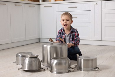 Photo of Little boy pretending to play drums on pots in kitchen