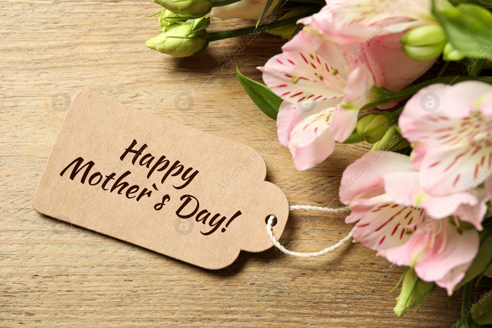 Image of Happy Mother's Day greeting label and beautiful flowers on wooden table