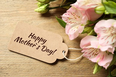 Image of Happy Mother's Day greeting label and beautiful flowers on wooden table