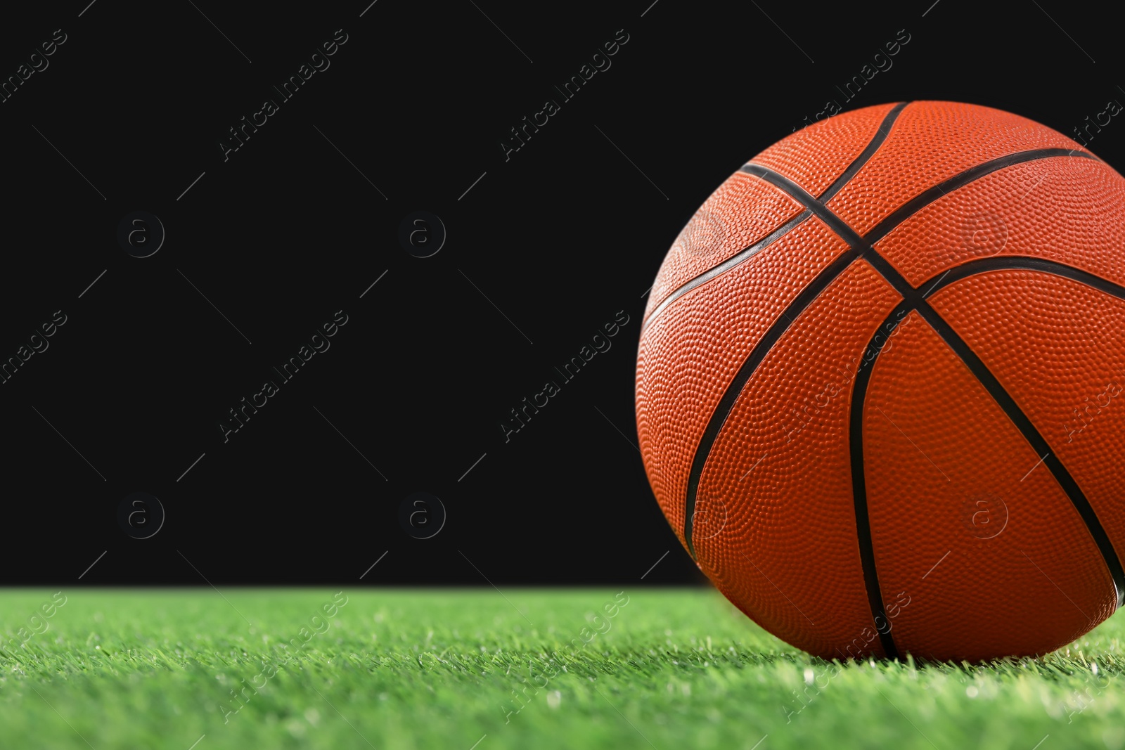 Photo of Basketball ball on green grass against black background, closeup. Space for text