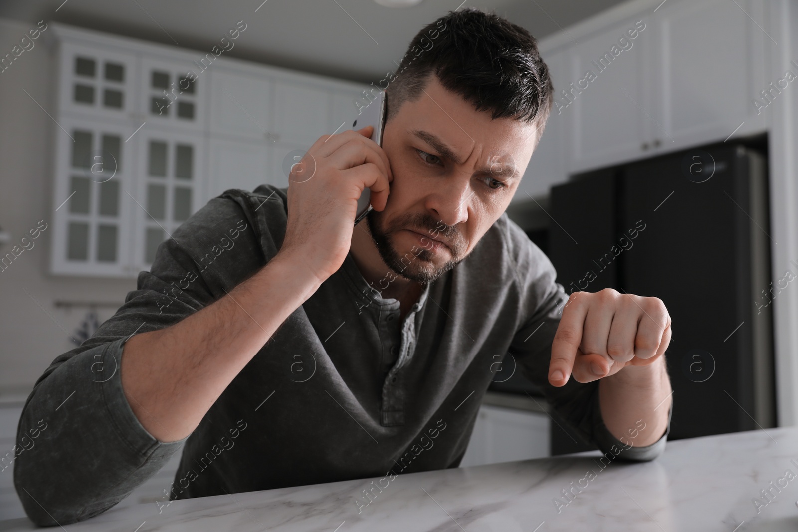 Photo of Emotional man talking on phone at table in kitchen. Hate concept
