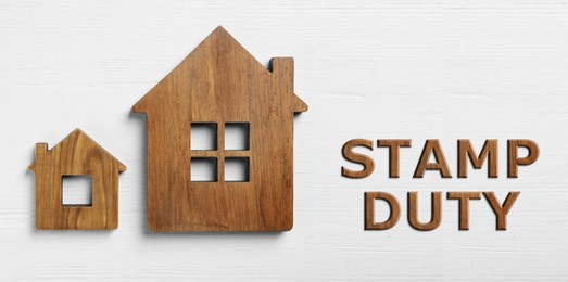 Image of Stamp duty. Small and big house figures on white wooden background, flat lay