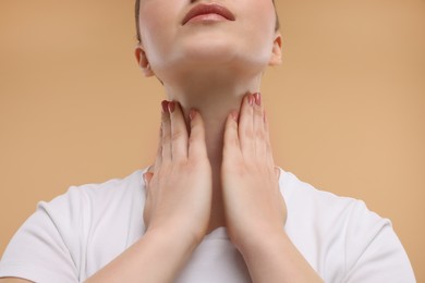 Woman touching her neck on beige background, closeup