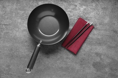 Empty iron wok and chopsticks on grey table, flat lay