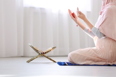 Muslim woman with beads praying on mat indoors