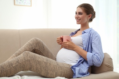 Happy pregnant woman drinking tea at home