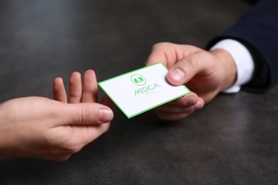 Man giving medical business card to woman on dark background, closeup. Nephrology service