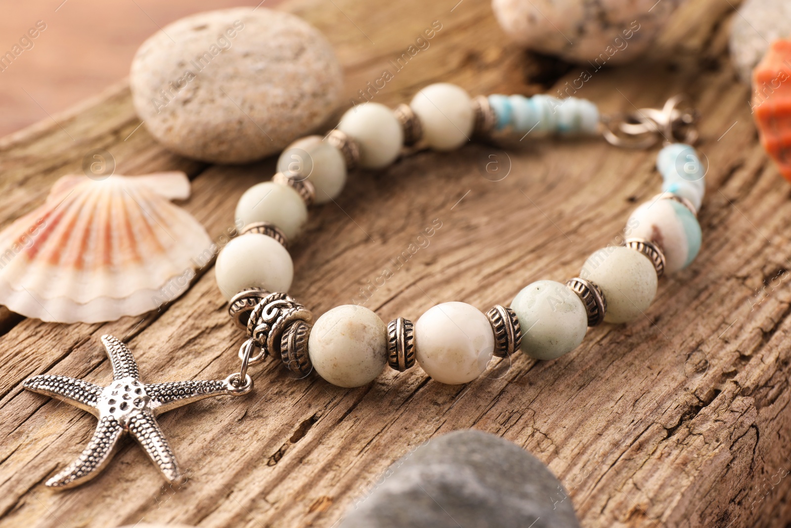 Photo of Beautiful bracelet with gemstones, stones and seashell on wooden surface, closeup