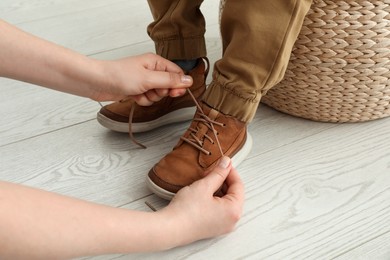 Mother helping son to tie shoe laces at home, closeup