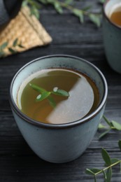 Photo of Cup of aromatic eucalyptus tea on black wooden table, closeup