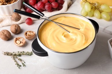 Photo of Pot of delicious cheese fondue and forks on gray table