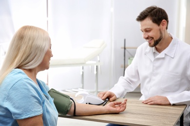 Doctor checking mature woman's pulse with medical device in hospital