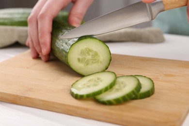 Photo of Woman cutting cucumber on wooden board at white table, closeup