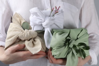 Photo of Furoshiki technique. Woman holding gifts packed in different fabrics decorated with plants, closeup