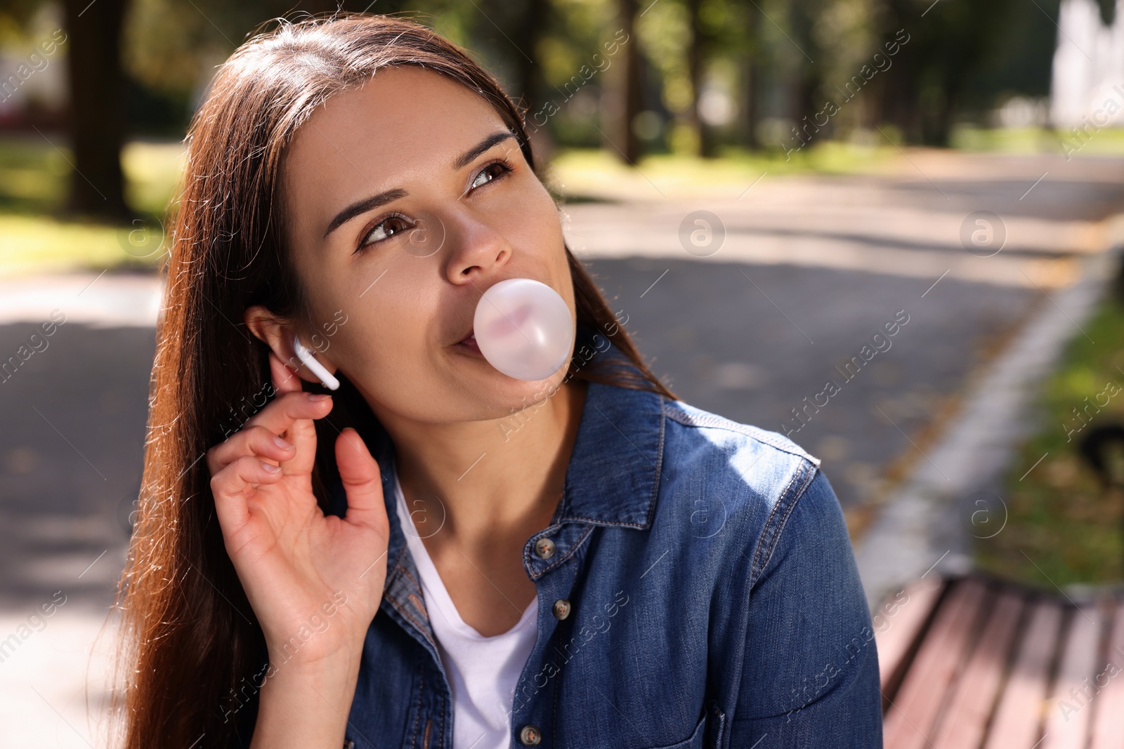 Photo of Beautiful young woman with wireless headphones blowing chewing gum outdoors