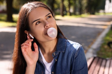 Photo of Beautiful young woman with wireless headphones blowing chewing gum outdoors