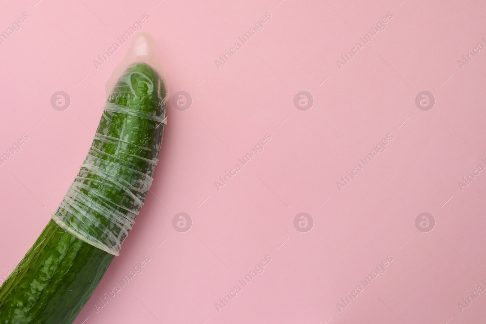 Photo of Cucumber with condom on pink background, top view and space for text. Safe sex concept
