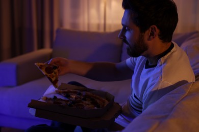 Man eating pizza while watching TV on sofa at night. Bad habit