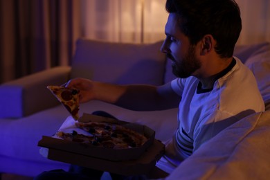 Photo of Man eating pizza while watching TV on sofa at night. Bad habit