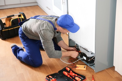 Photo of Male technician in uniform repairing refrigerator indoors