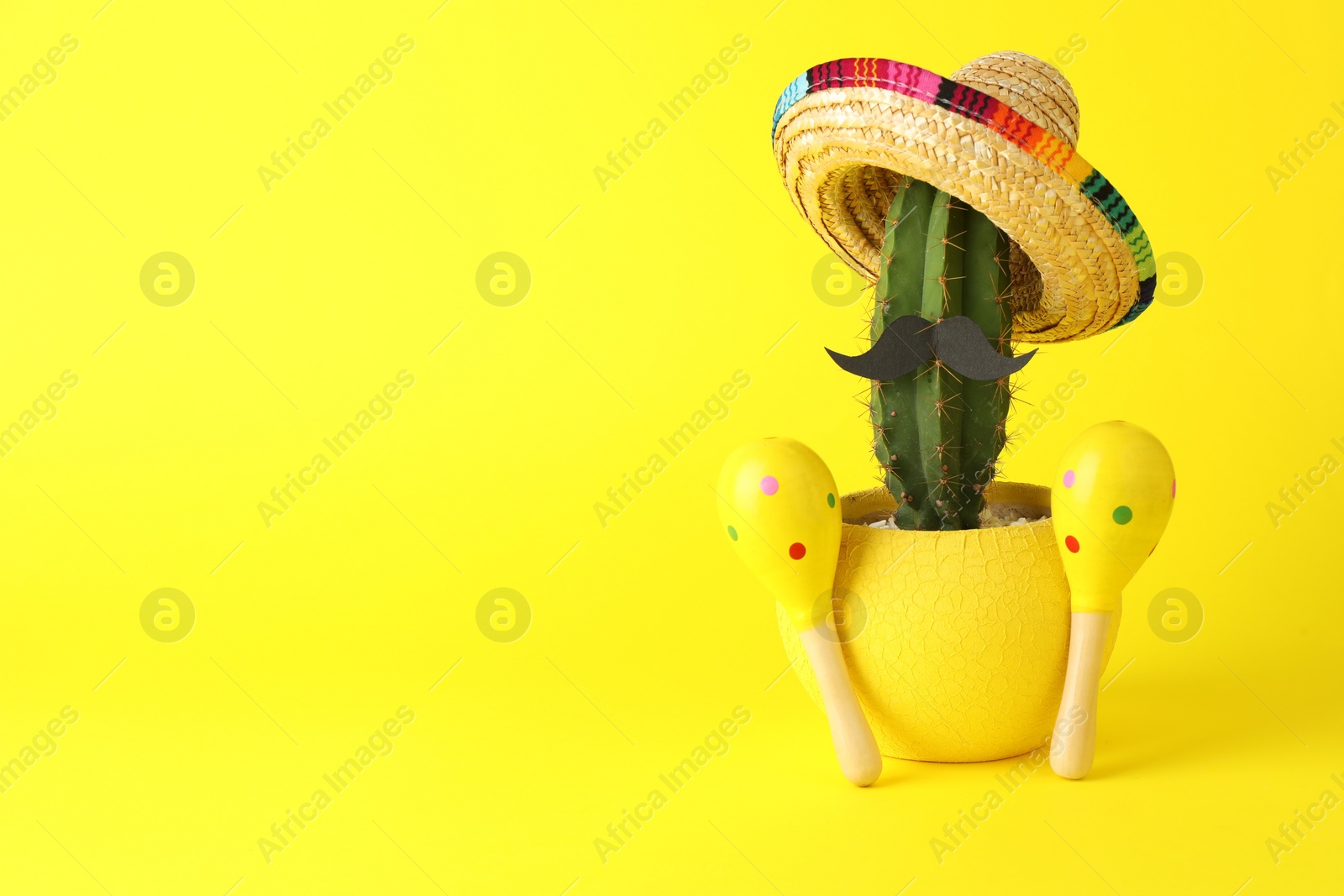 Photo of Cactus with Mexican sombrero hat, fake mustache and maracas on yellow background, space for text