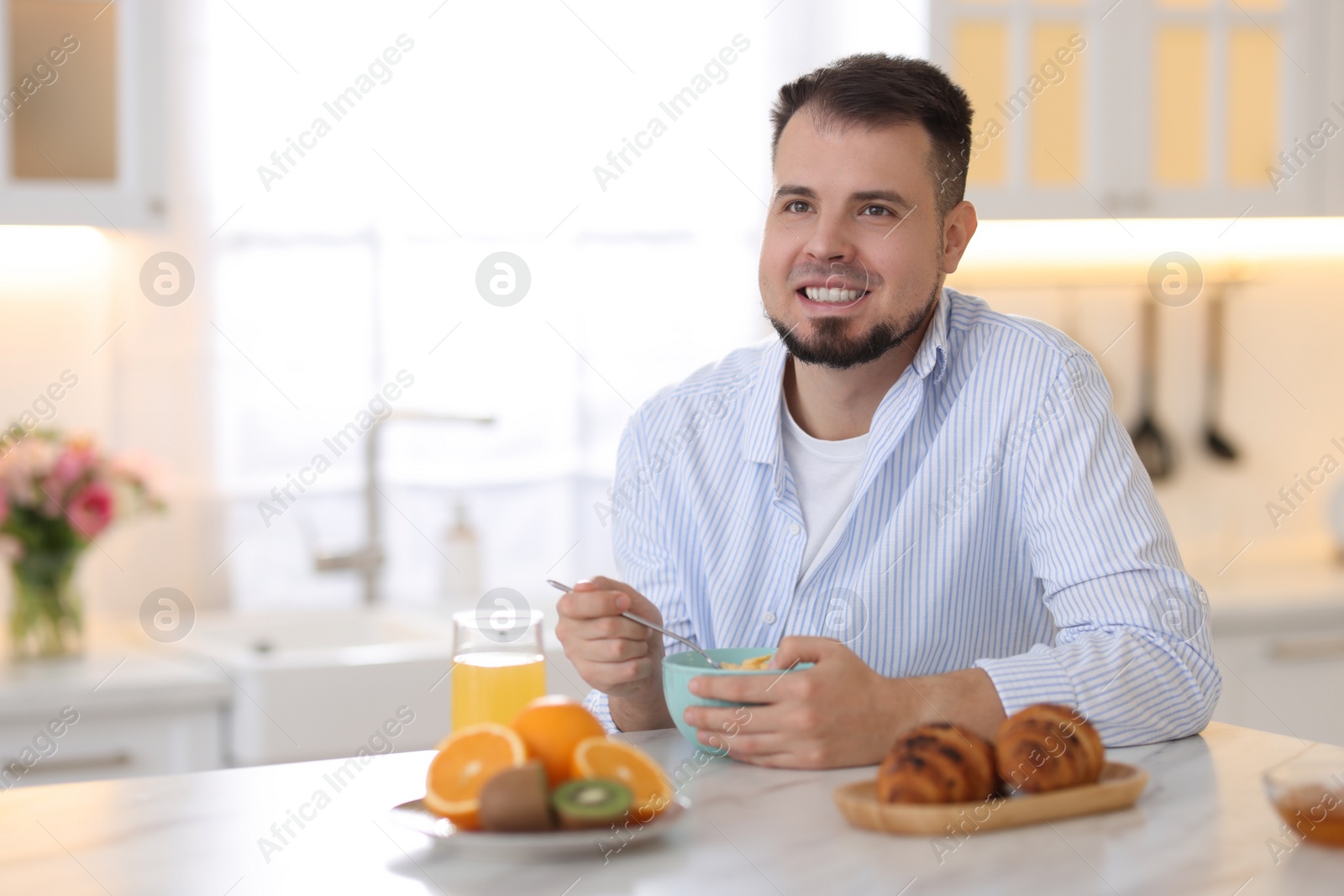 Photo of Smiling man eating tasty cornflakes at breakfast indoors. Space for text