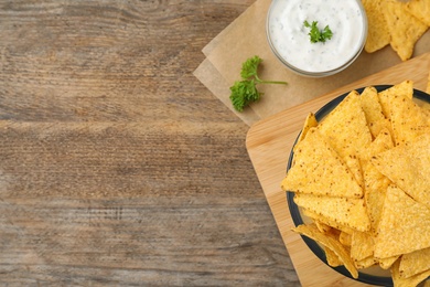 Mexican nacho chips with sauce on wooden background, flat lay. Space for text