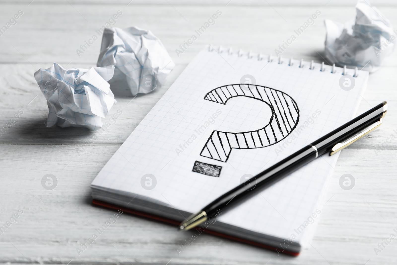 Photo of Notebook with question mark, pen and crumpled paper on white wooden table, closeup