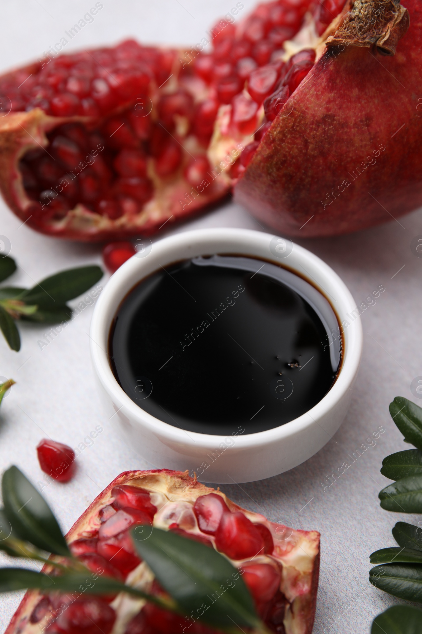 Photo of Tasty pomegranate sauce in bowl, branches and fruits on light table, closeup