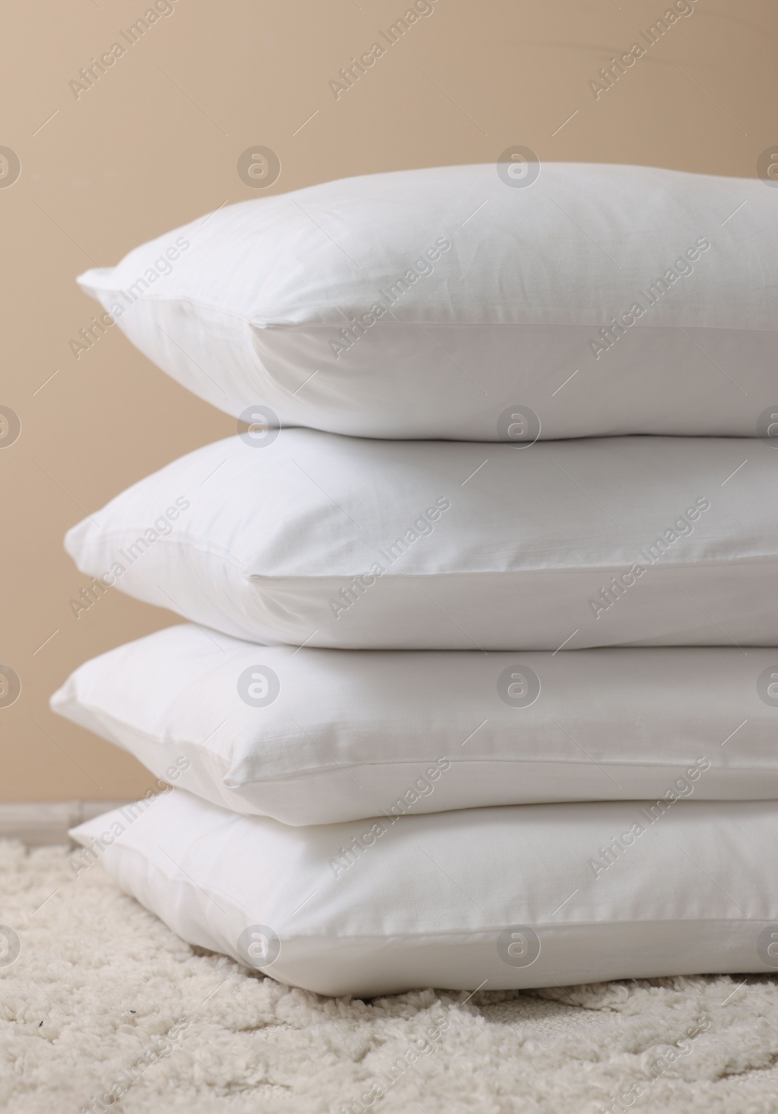 Photo of Stack of soft white pillows near beige wall indoors