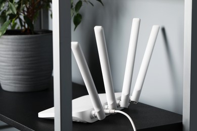 Photo of New white Wi-Fi router near potted plant on black shelf
