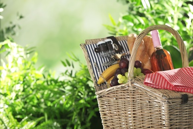Photo of Wicker picnic basket with different products on blurred background, space for text