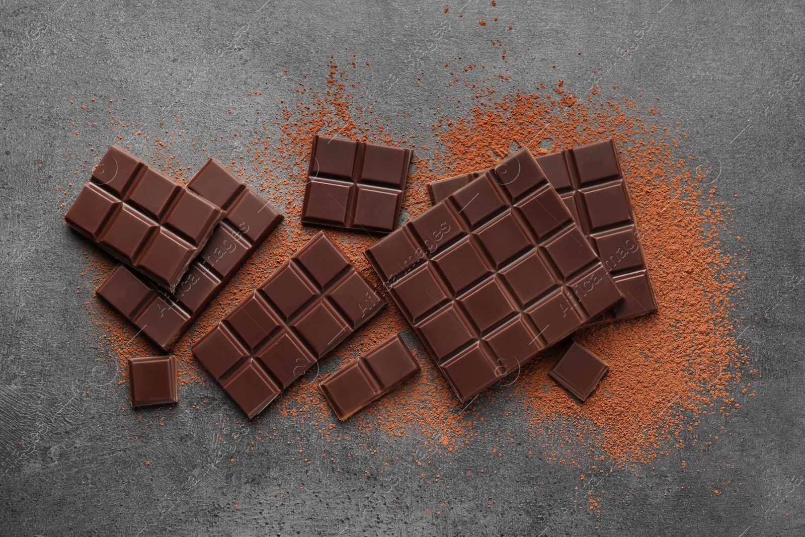 Photo of Delicious dark chocolate and cocoa powder on grey table, flat lay