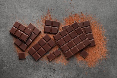 Photo of Delicious dark chocolate and cocoa powder on grey table, flat lay