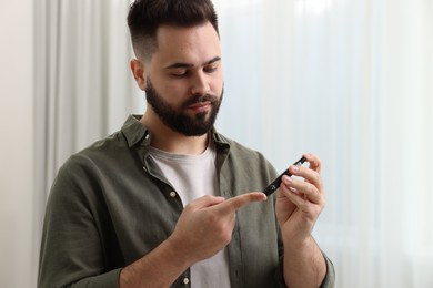 Photo of Diabetes test. Man checking blood sugar level with lancet pen at home