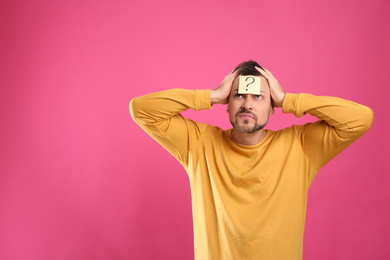 Photo of Emotional man with question mark on pink background, space for text