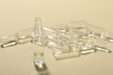 Photo of Glass ampoules with liquid on beige background, closeup